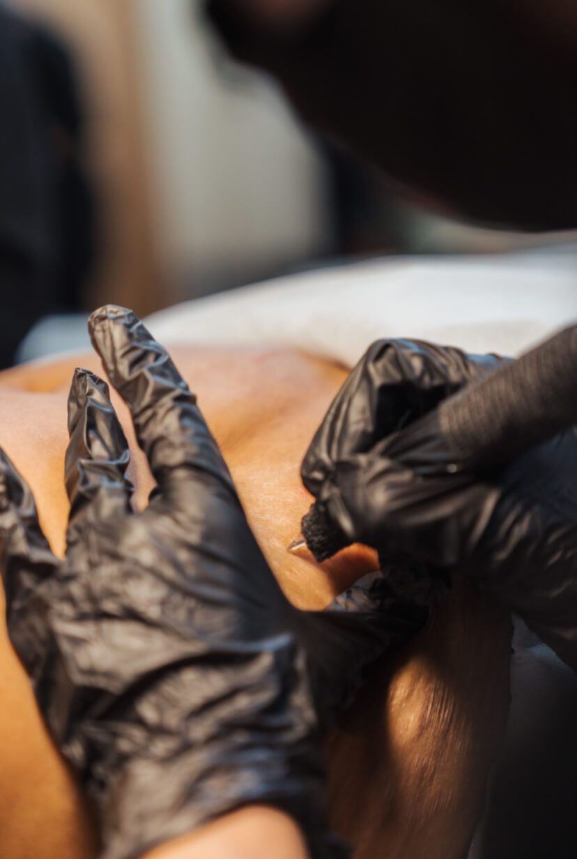 Person wearing black gloves tattooing another person's skin using a tattoo machine.