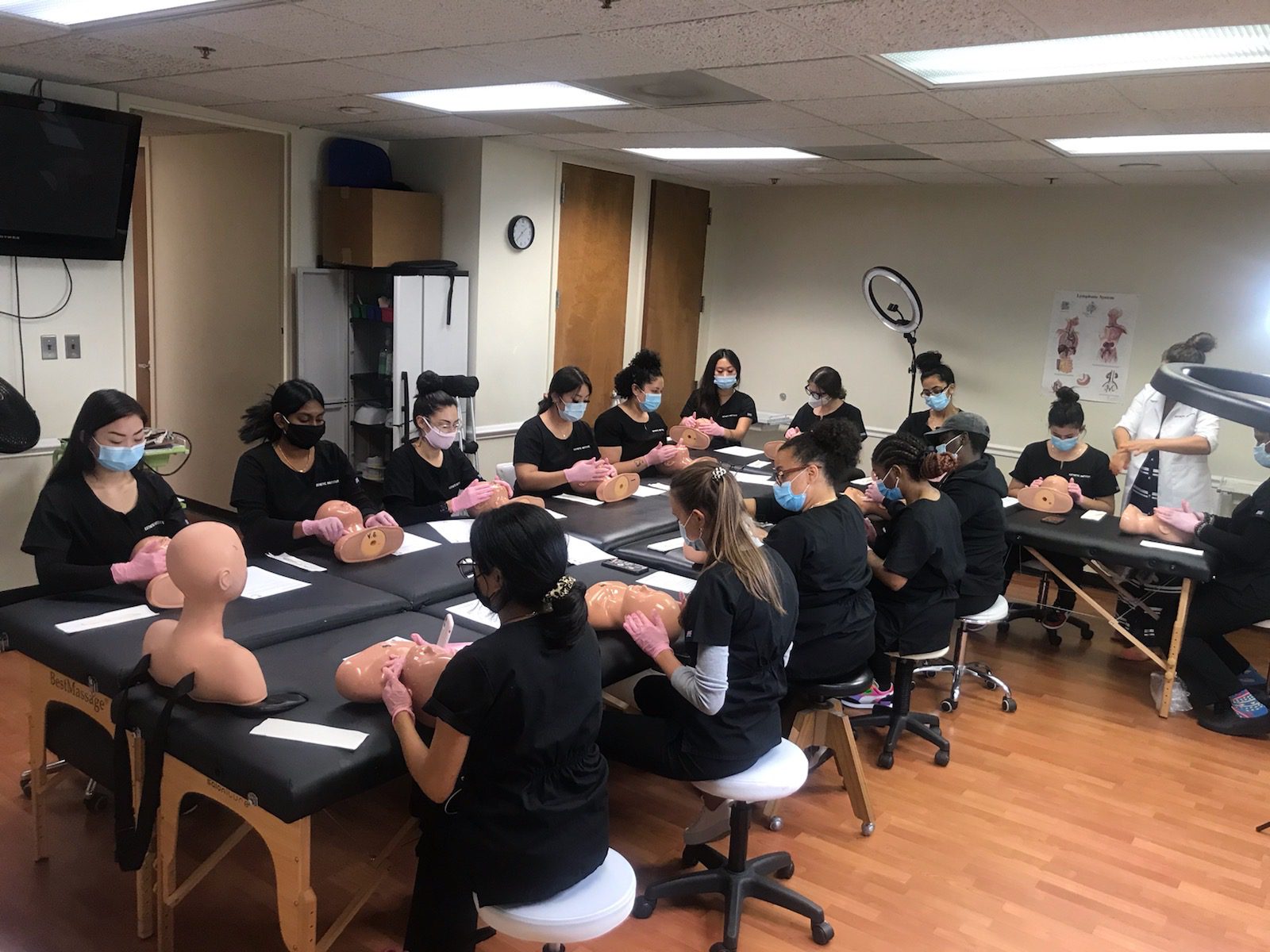 Room with people in black uniforms and masks practicing on mannequin heads at tables.