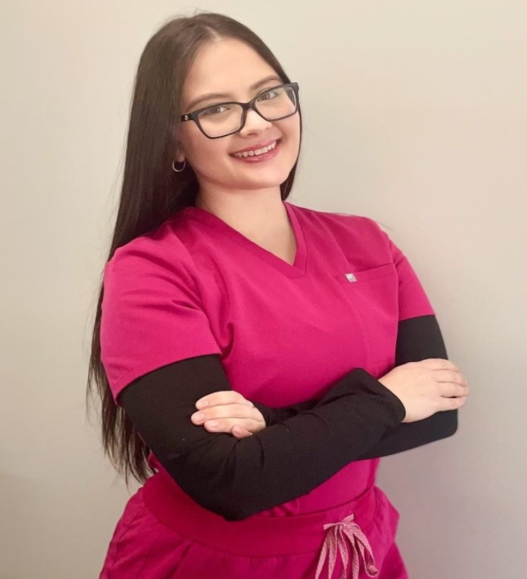 Mary-N-PMU-sm-1-1 A woman in pink scrubs standing with her arms crossed.