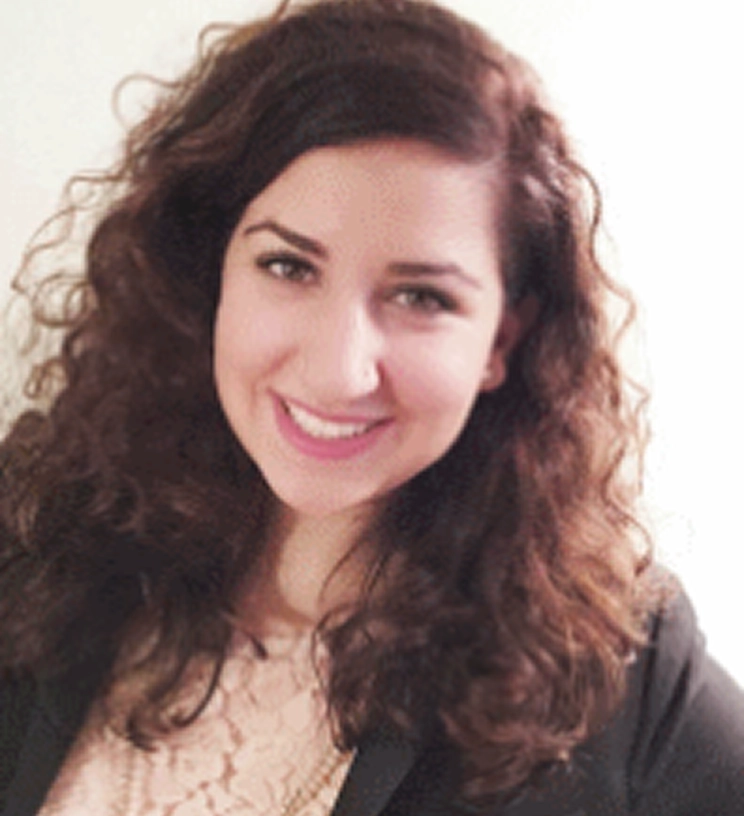 Woman with curly hair smiling, wearing a black blazer over a lace top, against a plain background.