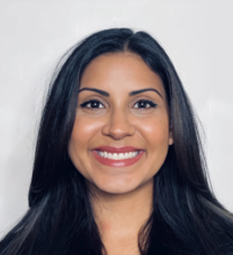 Smiling person with long dark hair, wearing a light-colored top, against a plain background.