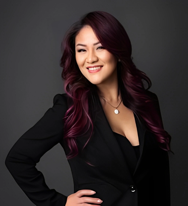 Woman with long, dark purple hair and a black outfit, smiling against a dark background.
