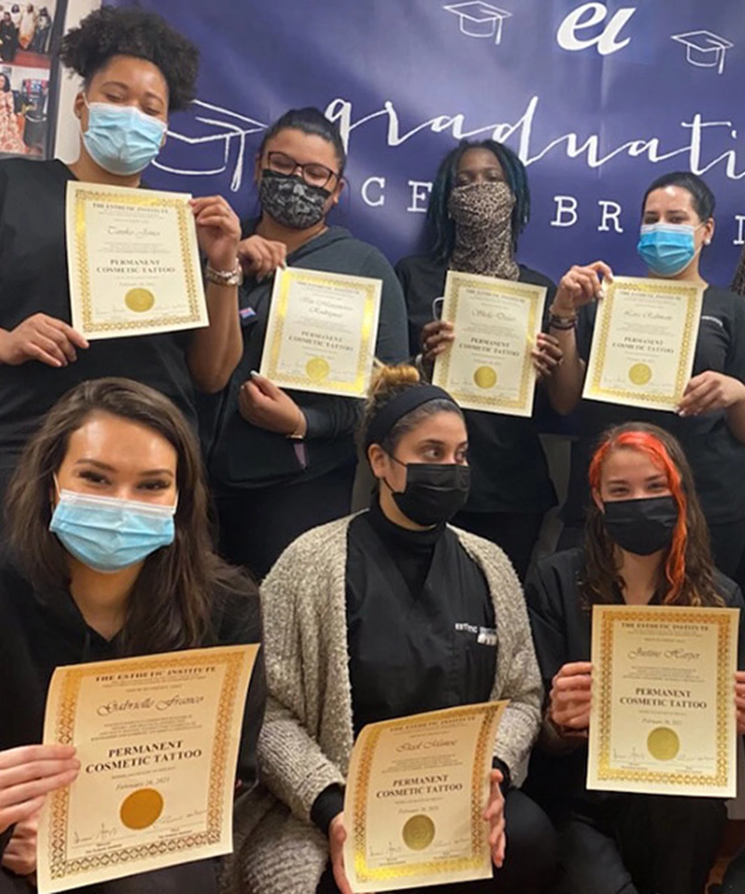 Seven people wearing masks hold certificates and pose in front of a blue banner with "graduation" written on it.
