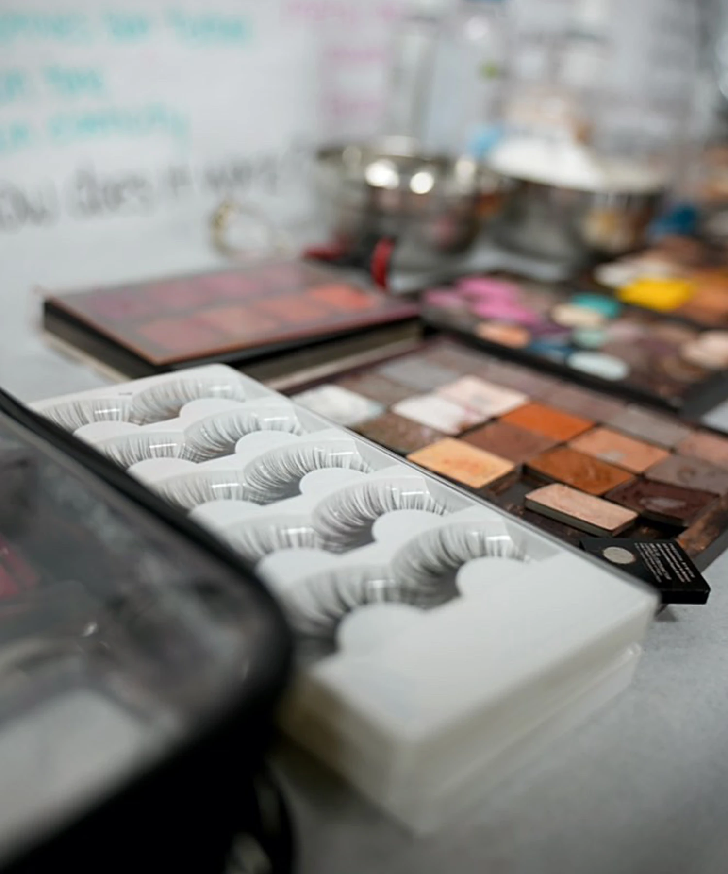 Boxes of false eyelashes and makeup palettes with various eyeshadow colors are arranged on a table.