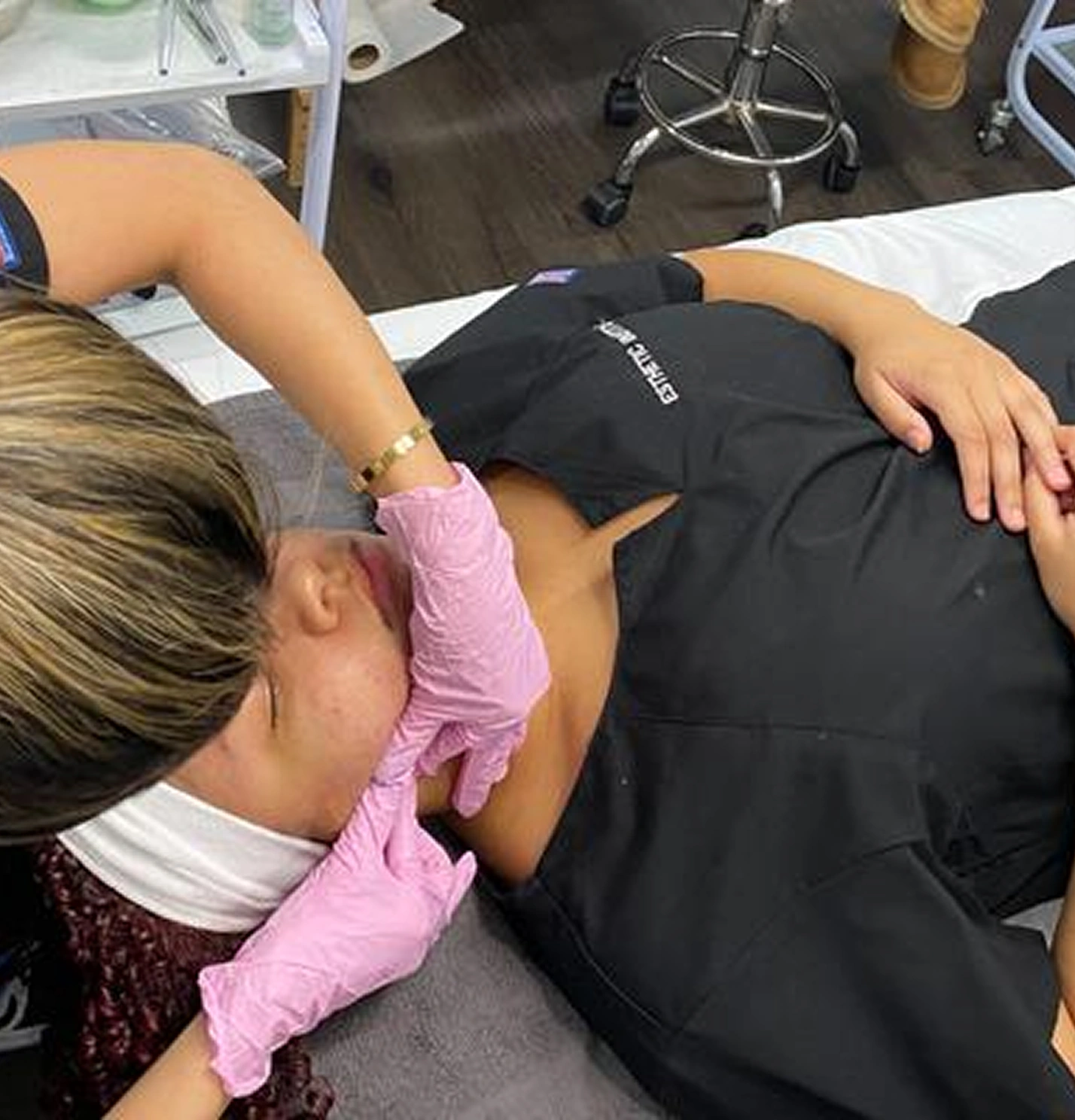 Person lying on a spa bed receiving a facial treatment from a professional wearing pink gloves.